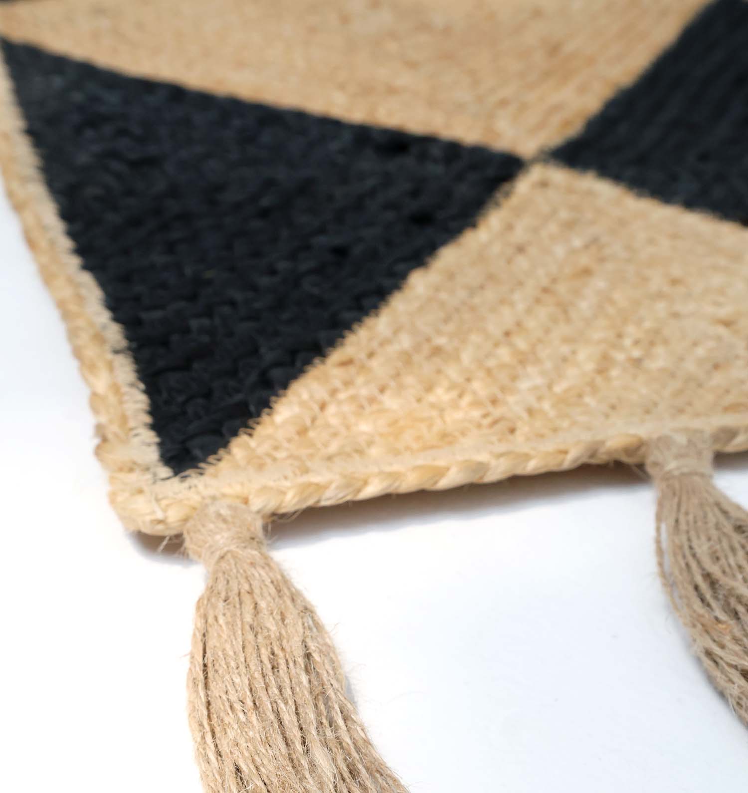 Close-up of the RAMSHA HOME Luxurious Handmade Natural & Black Color Jute Braided Rug with Tassel (BR 030), featuring a geometric triangle pattern, braided edges, and two beige tassels.