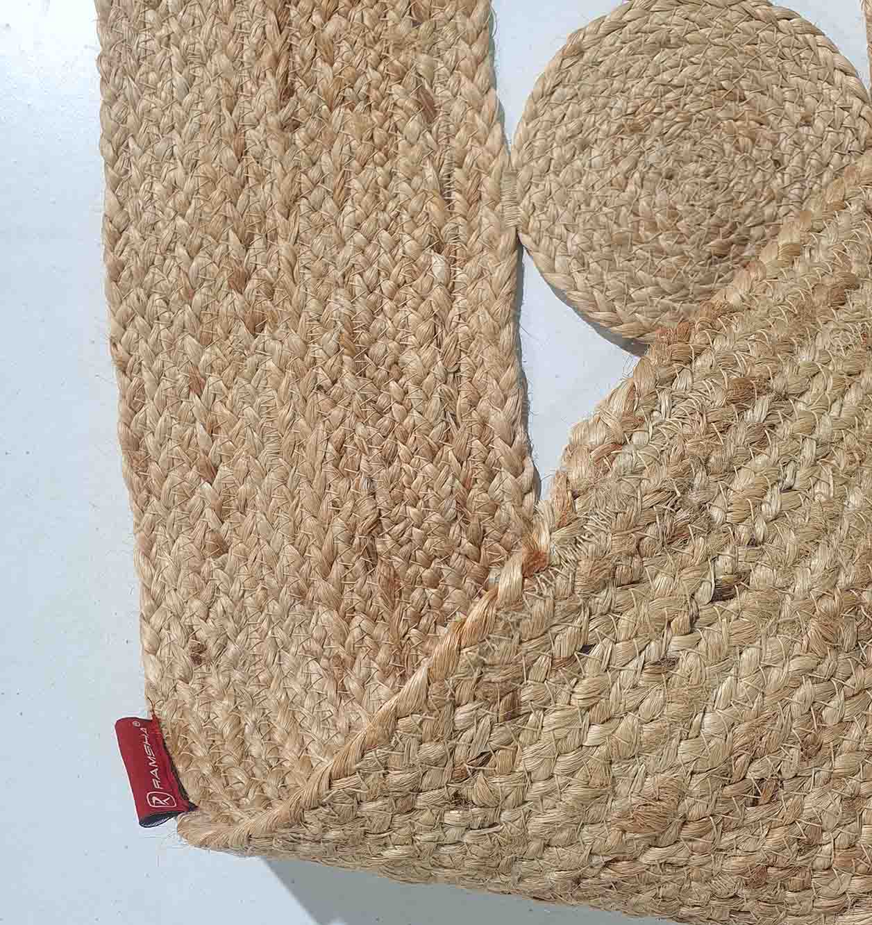 A close-up of RAMSHA HOME’s Beautiful Handmade Jute Floor Braided Rug - BR 032 shows one rectangular mat with a red tag and one small round mat, both featuring braided textures—ideal as decorative jute rug accents for any room.
