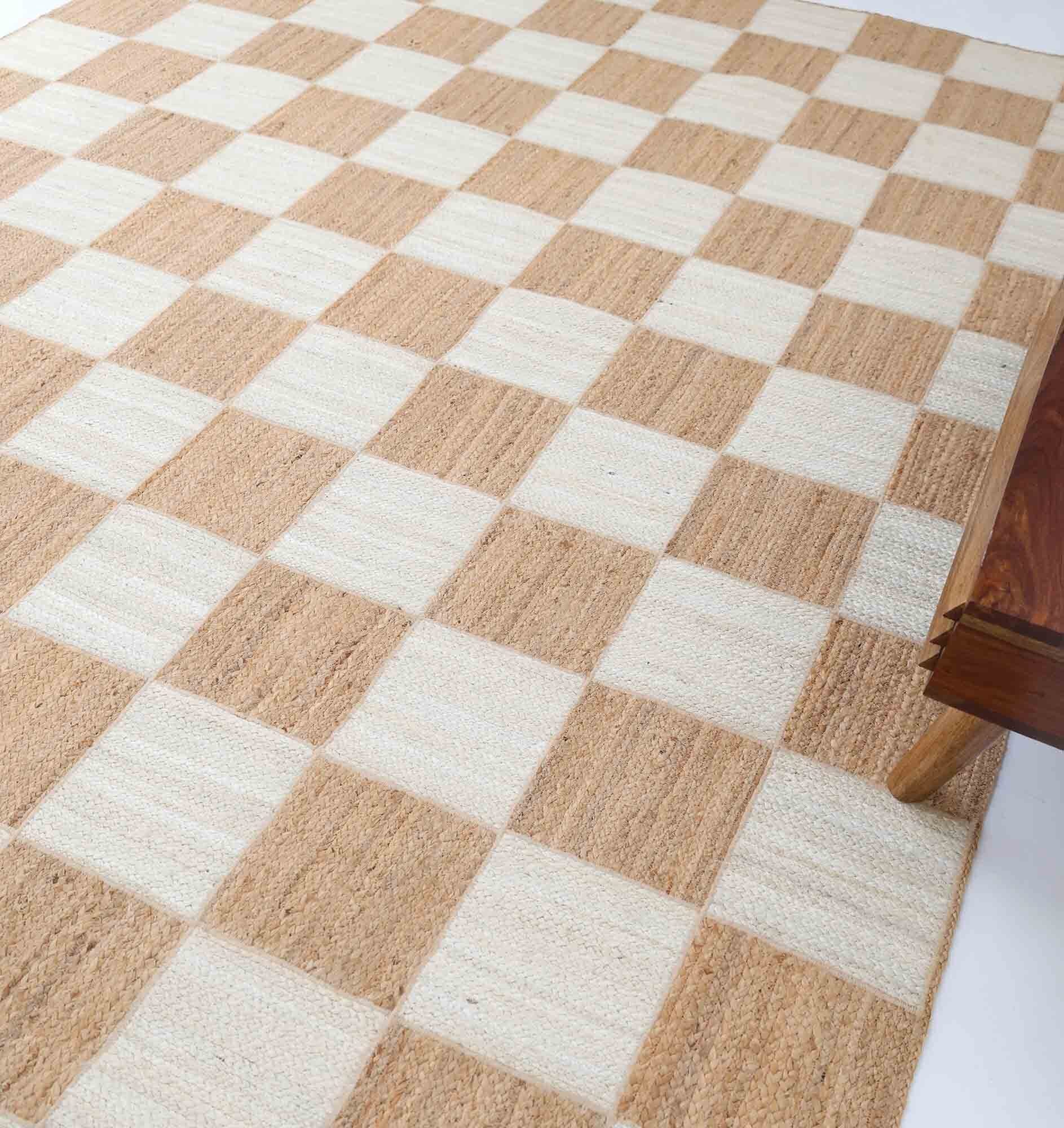 The Stunning Handmade Natural & Bleach Color Outdoor Jute Braided Rug - BR 037 by RAMSHA HOME is shown with its beige and off-white checkerboard pattern partially under a wooden table leg on the right side.