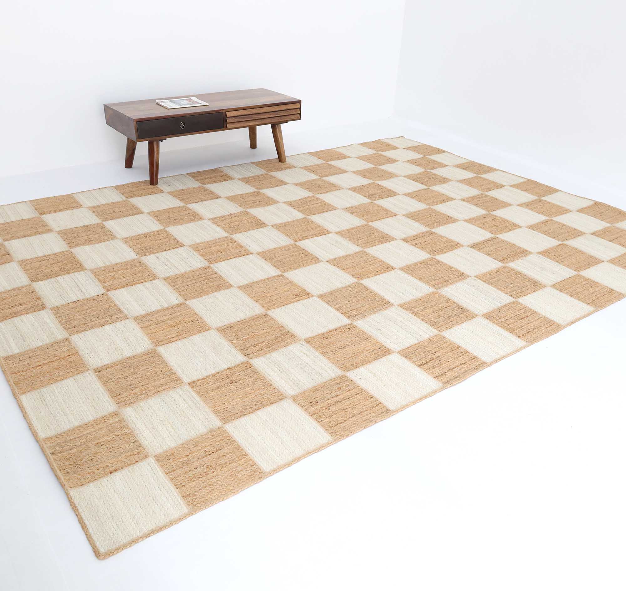 The Stunning Handmade Natural & Bleach Color Outdoor Jute Braided Rug - BR 037 by RAMSHA HOME lies on a white floor, paired with a wooden coffee table with angled legs and a drawer, adding modern style to the cozy space.