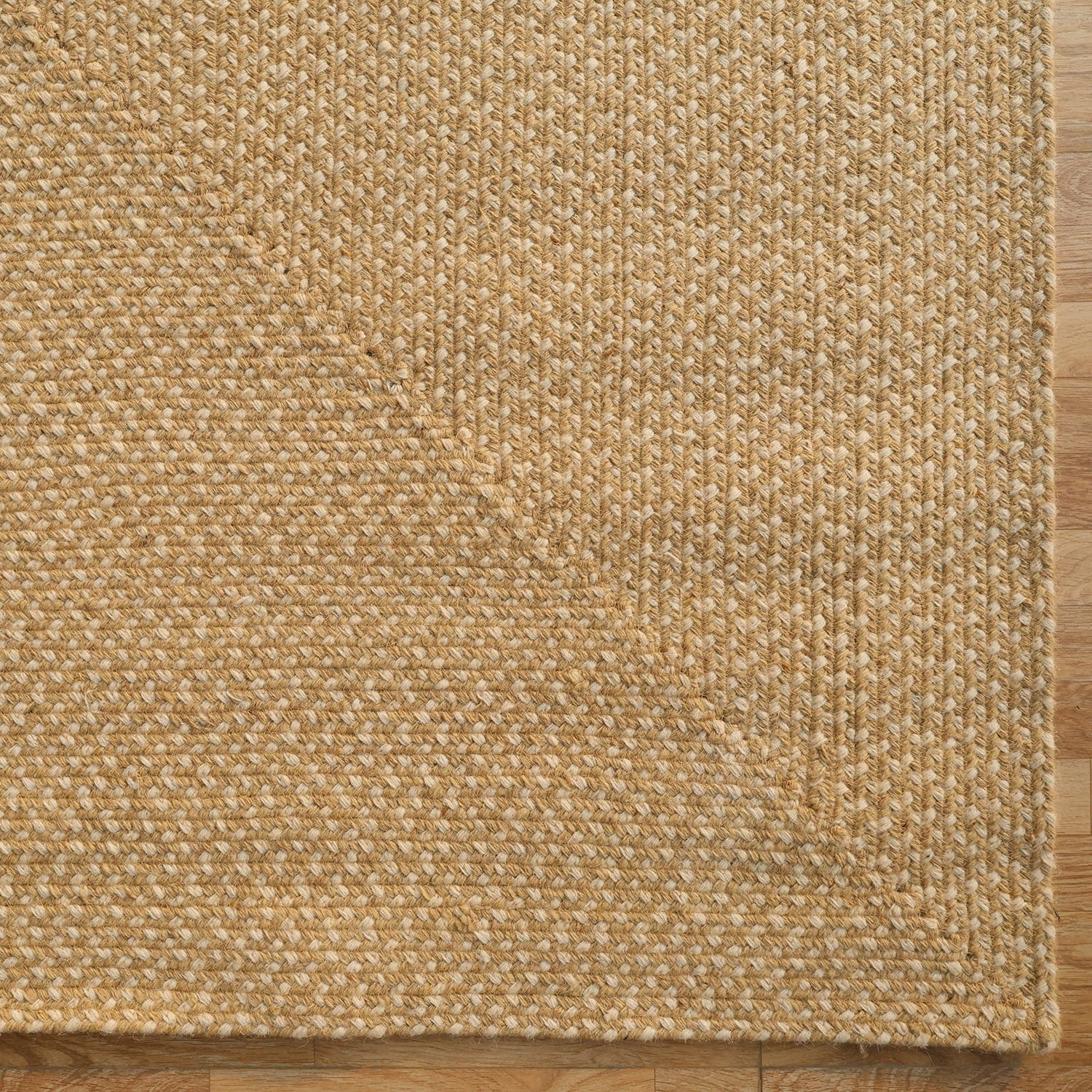A close-up of the RAMSHA HOME Natural Color Handmade Rectangle Wool Area Braided Rug - BR 053C on a wooden floor, highlighting its woven beige texture and braided pattern with a folded corner.