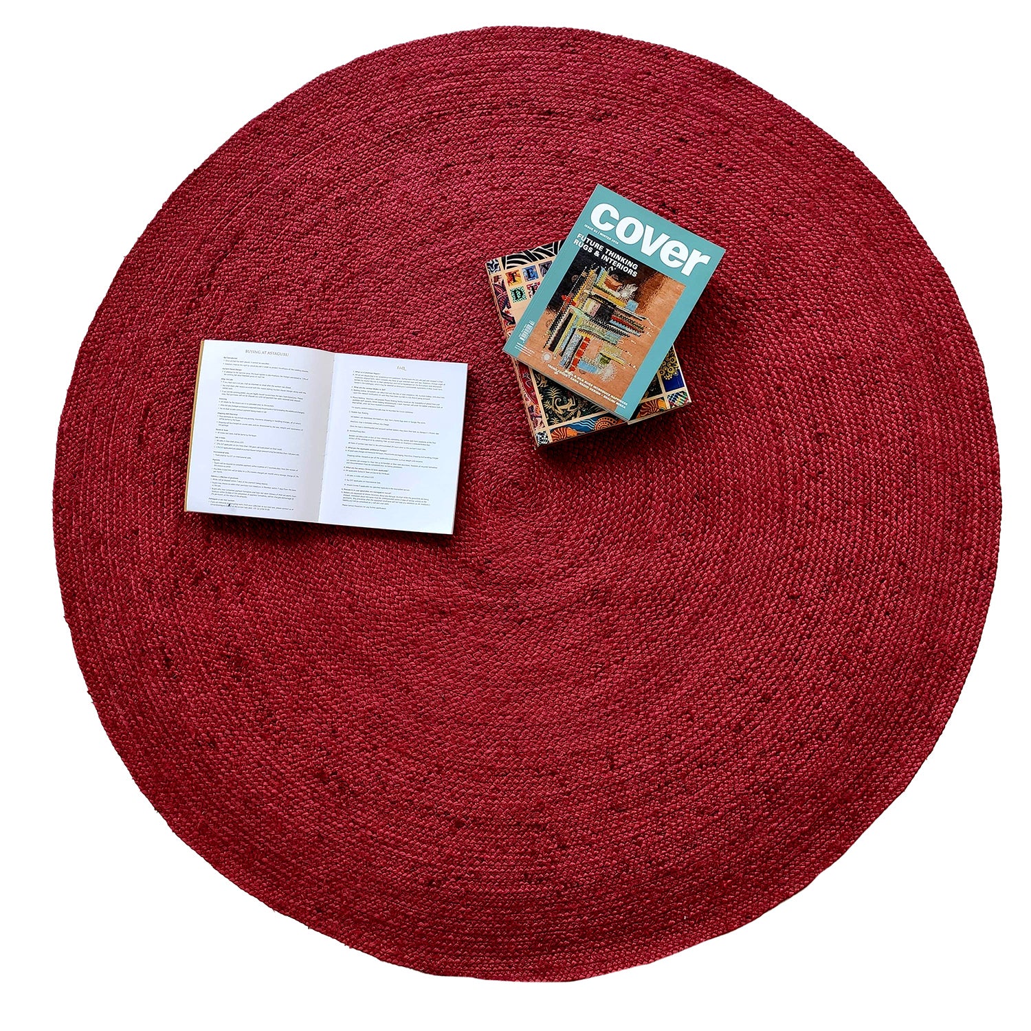 The RAMSHA HOME Jute Natural Rug Round Red Color BR-060 (90 cm) with a braided design is shown from above, featuring a few stacked books and an open book on top, set against a white background.