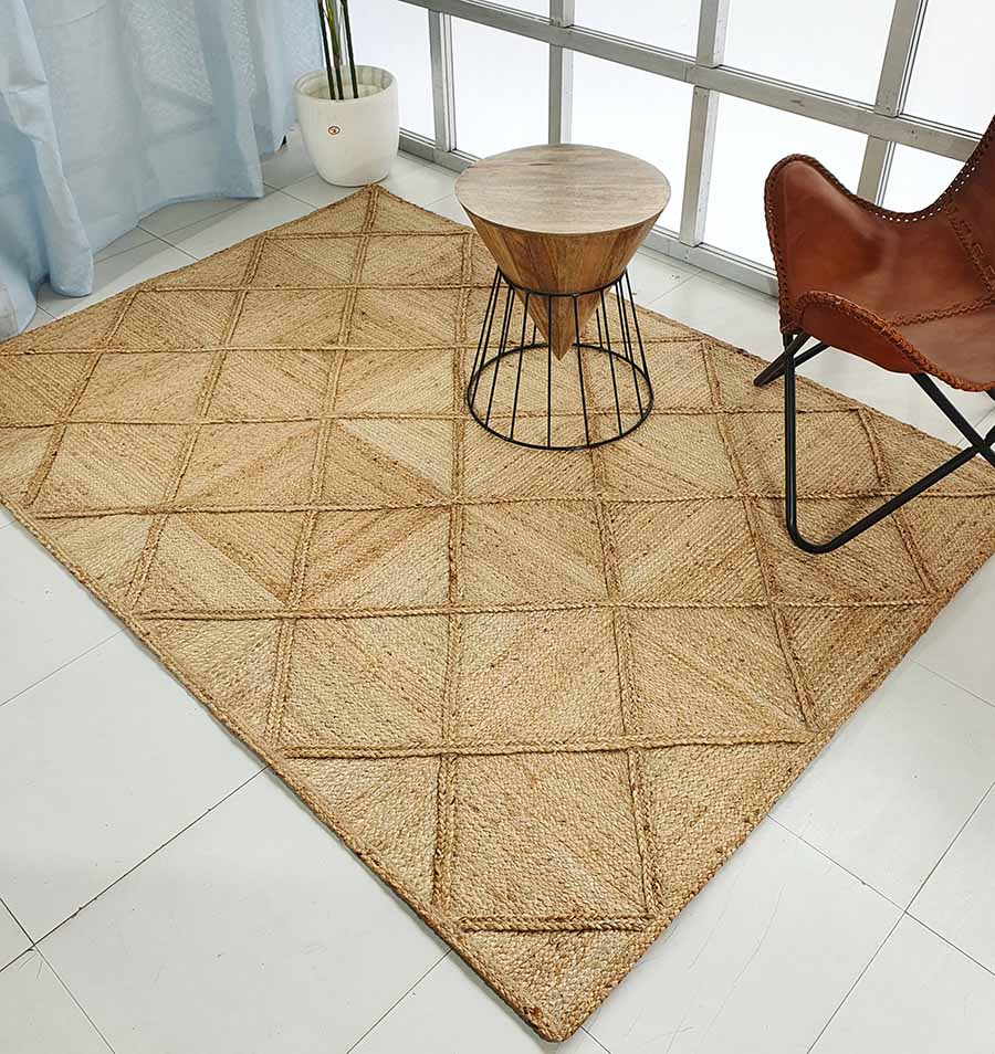 The RAMSHA HOME Amazing Handmade Jute Rug Living Room - BR 084 with a geometric diamond pattern lies on a white tile floor, paired with a round wooden table, brown leather chair, potted plant, and large windows in the background.