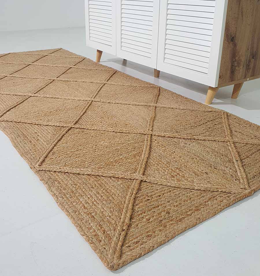 The RAMSHA HOME Amazing Handmade Jute Rug Living Room - BR 084 with a diamond pattern is placed on a white floor in front of a cabinet with white slatted doors and wooden legs.
