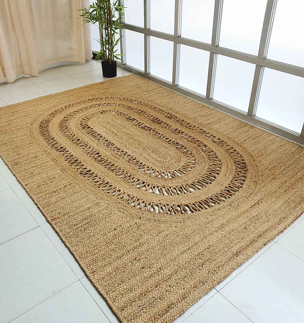 The Exquisite Braided Circle Jute Rug - BR 085 from RAMSHA HOME adds organic charm to a white tiled floor by the window, complemented by a potted bamboo plant in the corner and sheer curtains softly filtering the light.