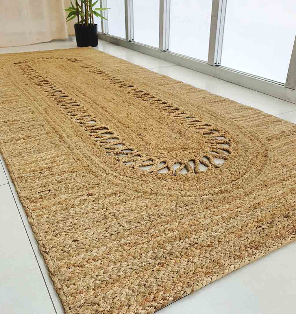 The RAMSHA HOME Exquisite Braided Circle Jute Rug - BR 085 adds natural style to a white tile floor by a large window, complemented by a potted plant near the curtains.