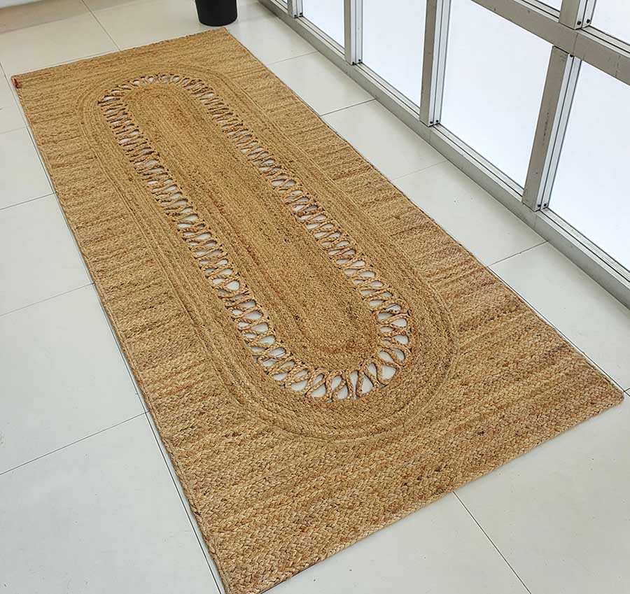 The Exquisite Braided Circle Jute Rug - BR 085 by RAMSHA HOME is displayed on a white tiled floor beside large windows.