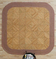 The RAMSHA HOME Natural & Rust Color Braided Outdoor Rug - BR 094 rests on a light wood floor. A small round black table with magazines sits at the bottom center edge of the rug.