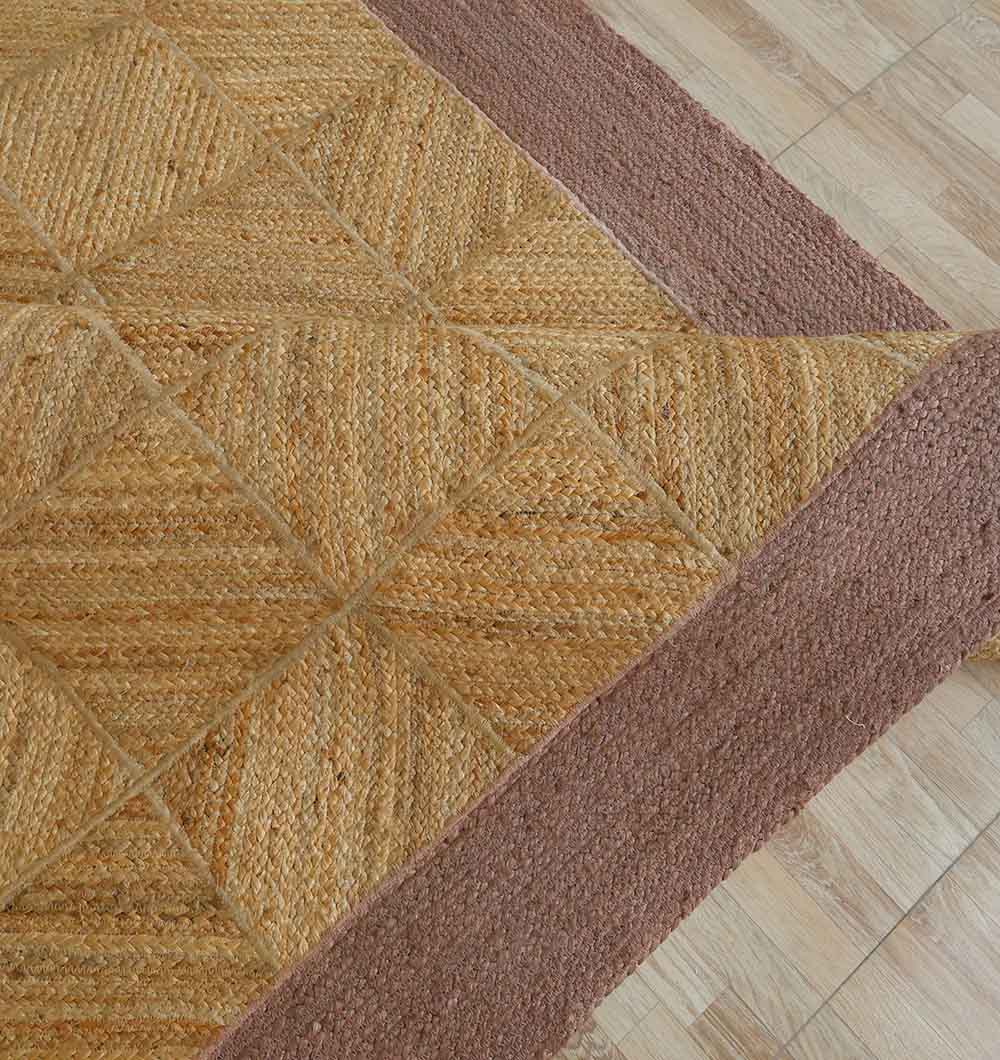 A close-up of the RAMSHA HOME Natural & Rust Color Braided Outdoor Rug - BR 094 with a geometric triangle pattern and wide brown border, shown on a light wooden floor.