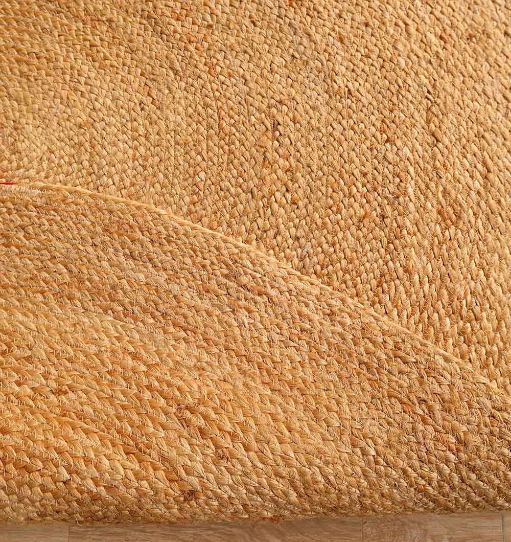 A close-up of the RAMSHA HOME Round Jute Rug Natural Color - BR 098, with one corner folded, highlights its textured natural fiber surface on a wooden floor.