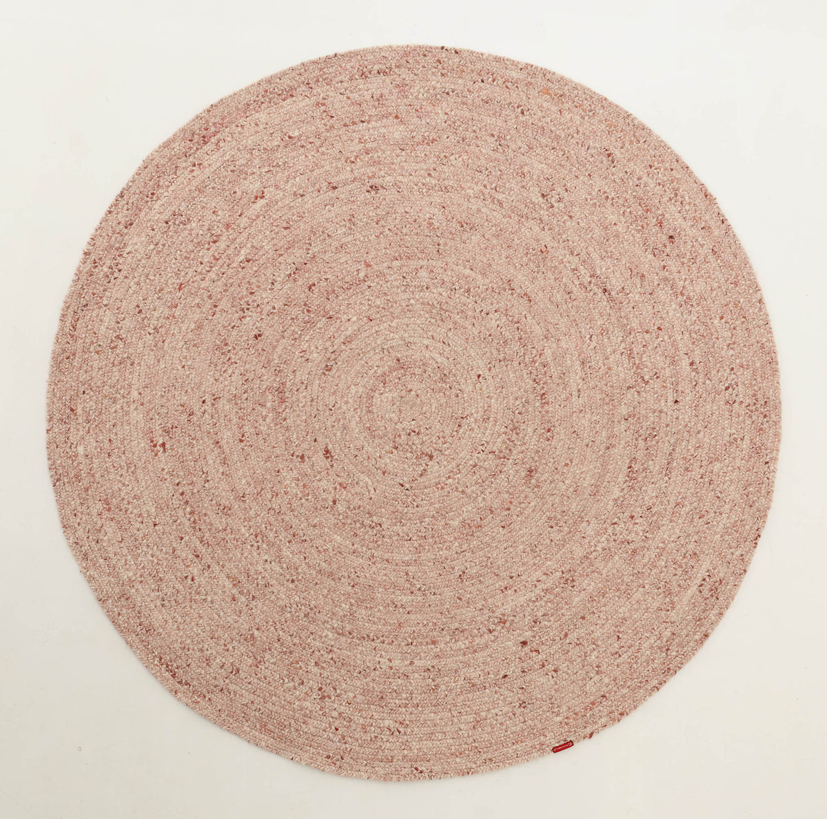 The Soft Pink Braided Wool Area Rug Handmade Circular Rug - BR 099 from RAMSHA HOME is a blush pink, round rug handcrafted from braided wool. Showcasing a delicate spiral pattern and minimalist design, this elegant piece is displayed against a plain white background, highlighting its gentle hue and refined texture.