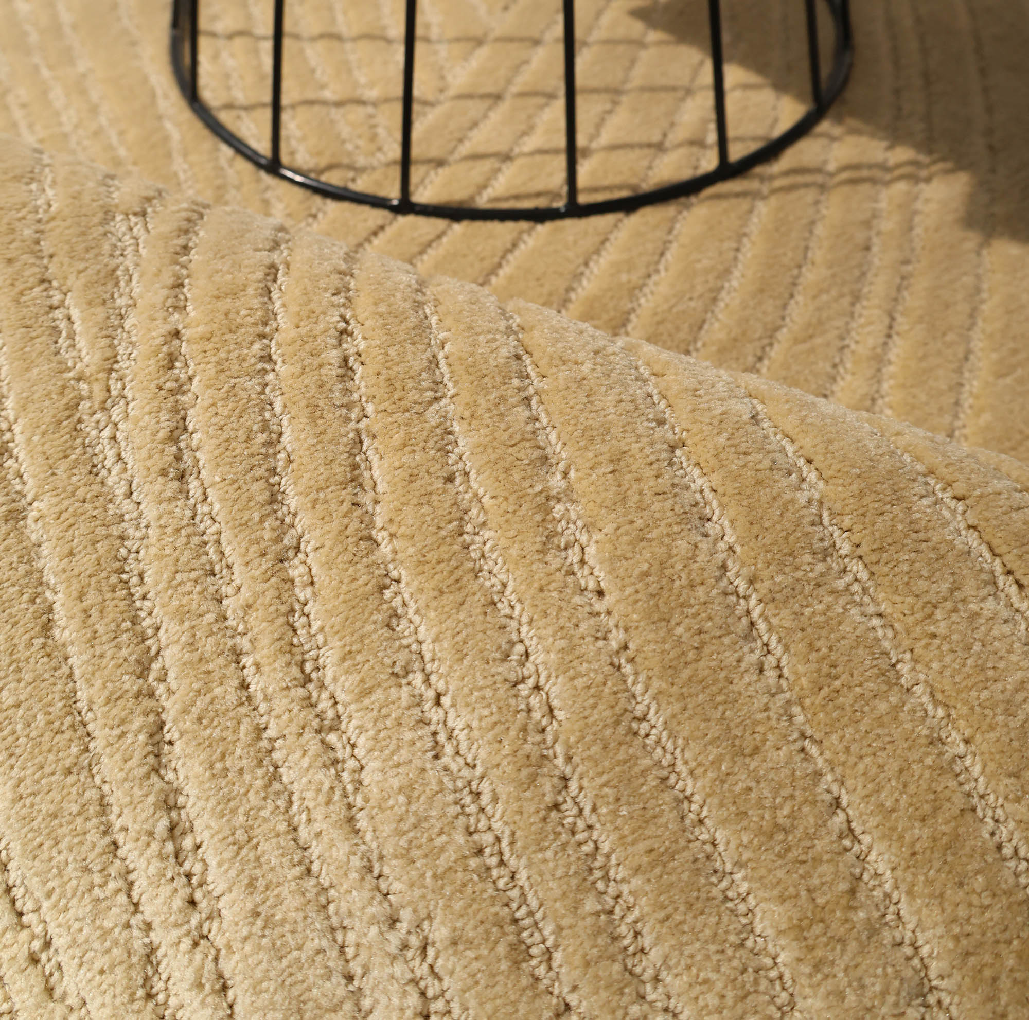 Close-up of the RAMSHA HOME Modern Terrain Round Shaped Rug CMN 114 in beige, featuring diagonal raised lines and partially covered by a metal wire circular base casting shadows on its textured surface.