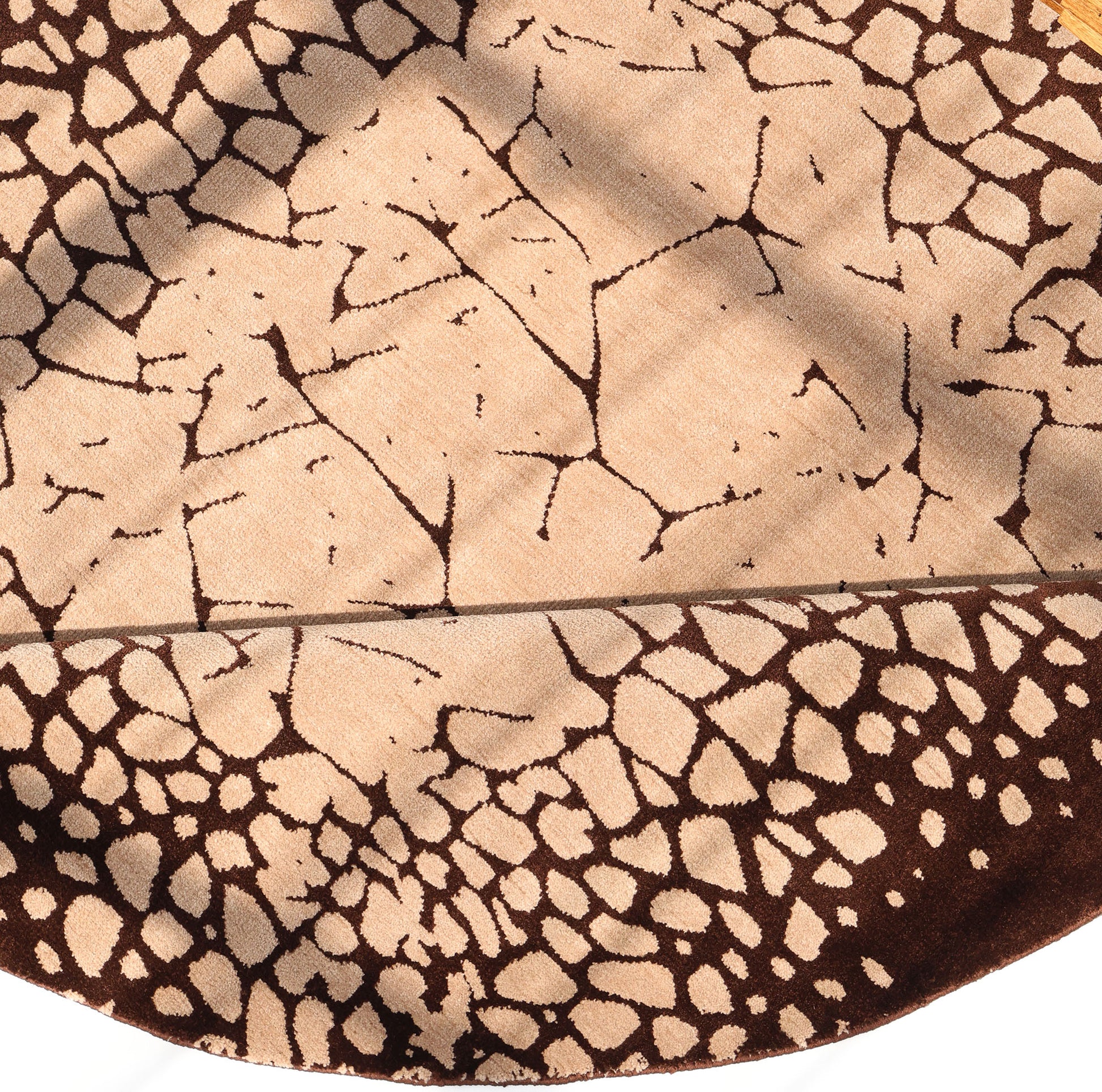 The RAMSHA HOME Terrain Echo Abstract Rug Shaped Rug CMN 118 features a handcrafted round design with a beige and dark brown cracked earth pattern, highlighted in natural sunlight with shadows on its modern surface.