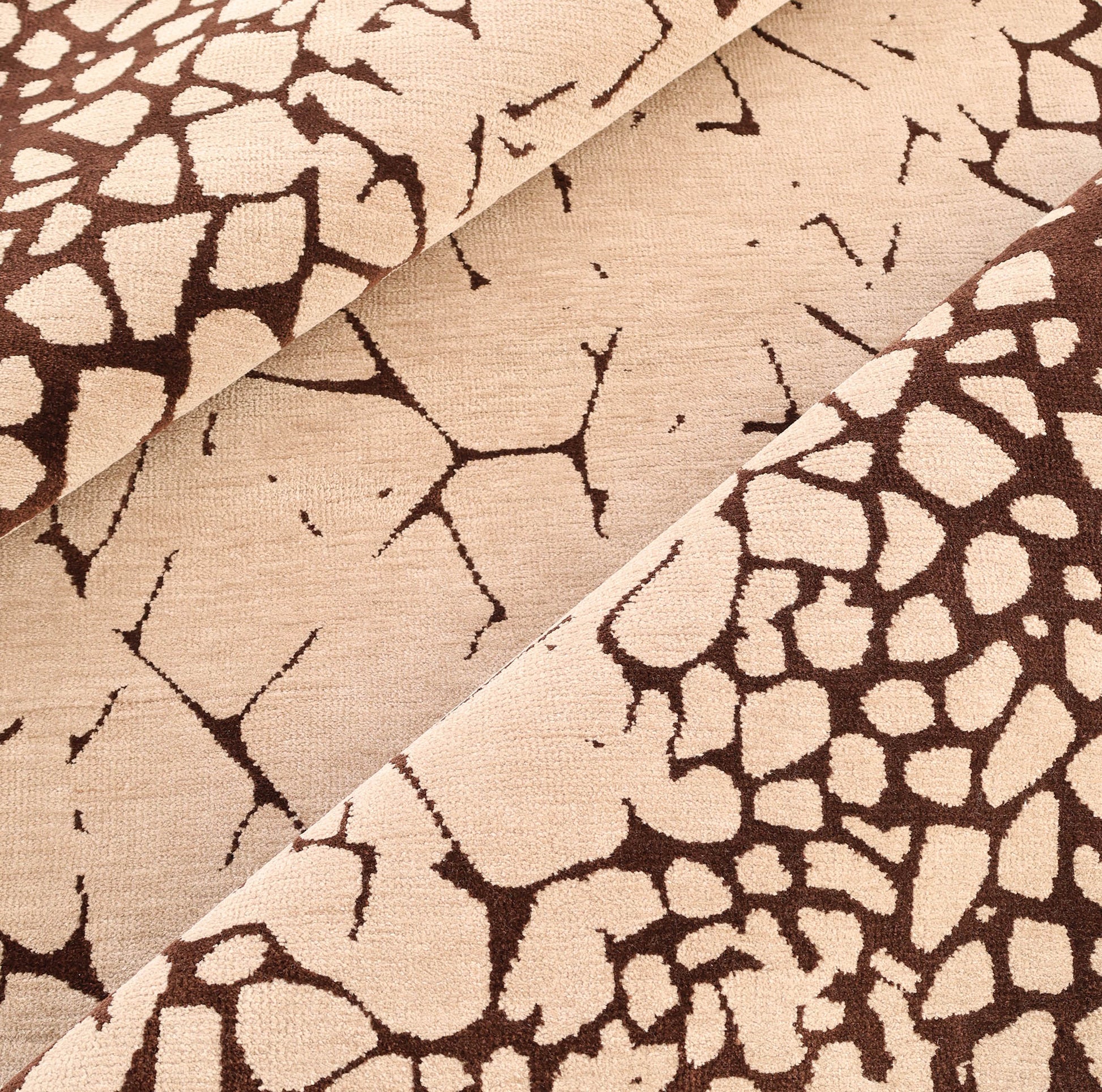 Close-up of the RAMSHA HOME Terrain Echo Abstract Rug Shaped Rug CMN 118, featuring a beige background with an irregular dark brown pattern reminiscent of giraffe spots or cracked earth, arranged in diagonal folds for a modern look.