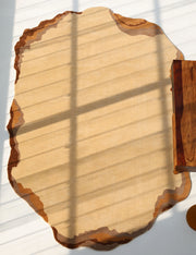 The Earth Layers Contemporary Rug Shaped Rug CMN 119 by RAMSHA HOME, in beige and brown with an organic silhouette, rests on a white floor patterned with window shadows. A wood-grain table appears partially on the right.