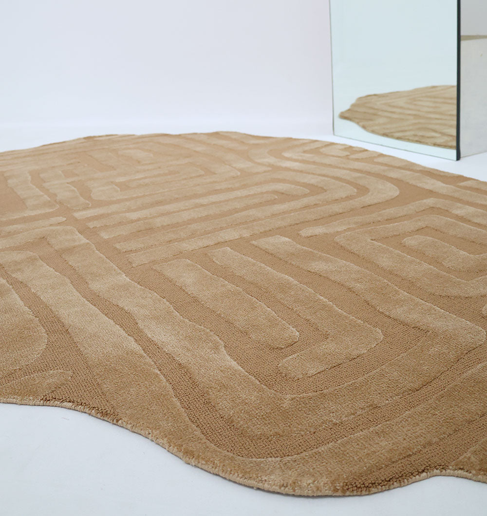 The RAMSHA HOME Amazing Brown Color Unshape Decor Rug- CMN 26 (200x300cm) with a textured, abstract design and curved edges lies on a white floor near a mirror, its unique form beautifully reflected in the glass.