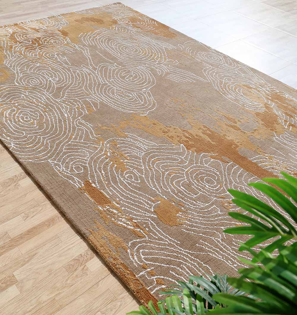 The RAMSHA HOME Multi Color Novara Decor Rug - CMN 33 (205X310cm) features tan and brown abstract swirls with white patterns, shown on a light wood floor with green leafy plants in the corner.