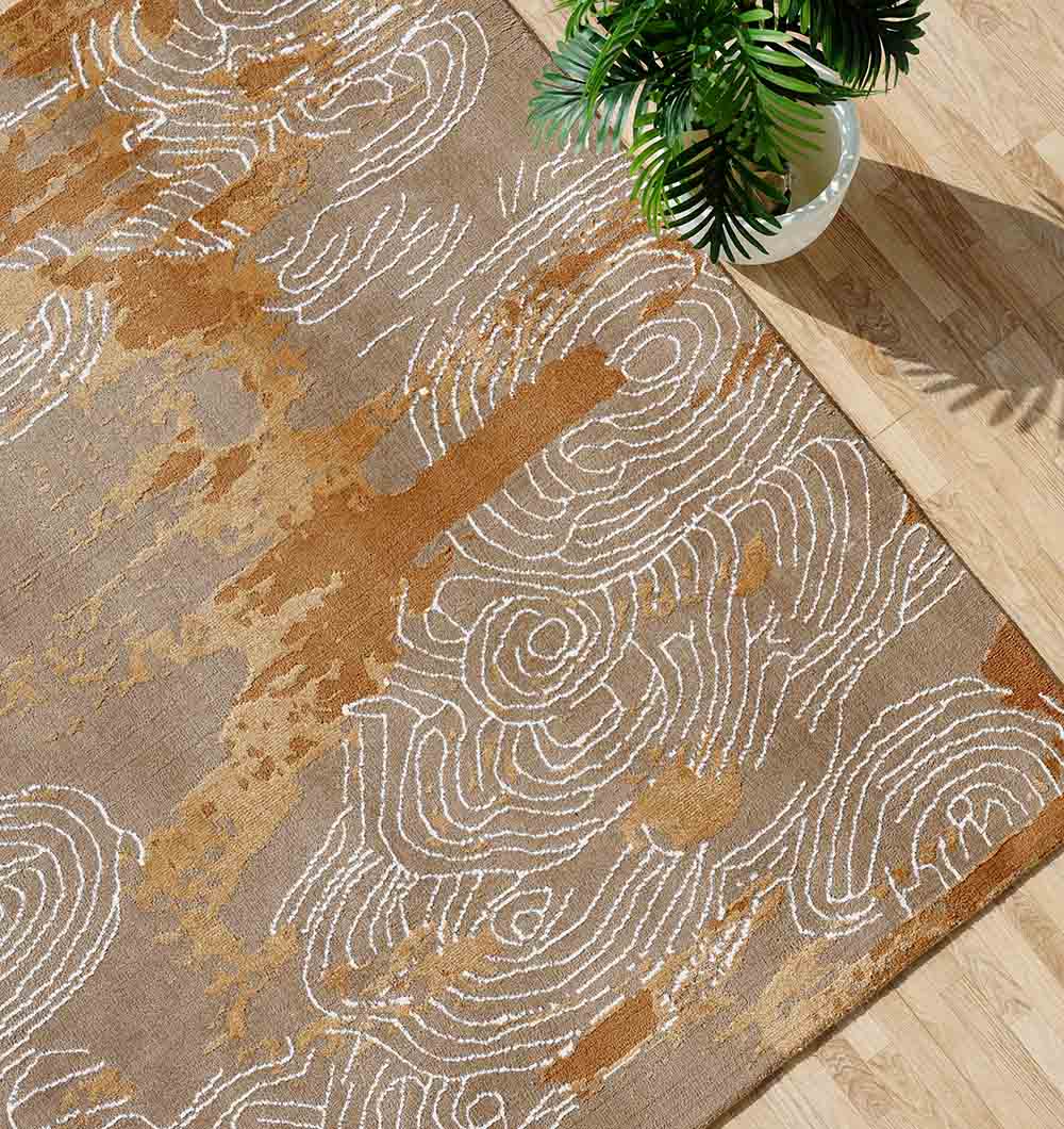 The RAMSHA HOME Multi Color Novara Decor Rug - CMN 33 (205X310cm) with brown, beige, and gold abstract swirl patterns lies on a light wood floor. A green potted plant in the top right casts a gentle shadow.