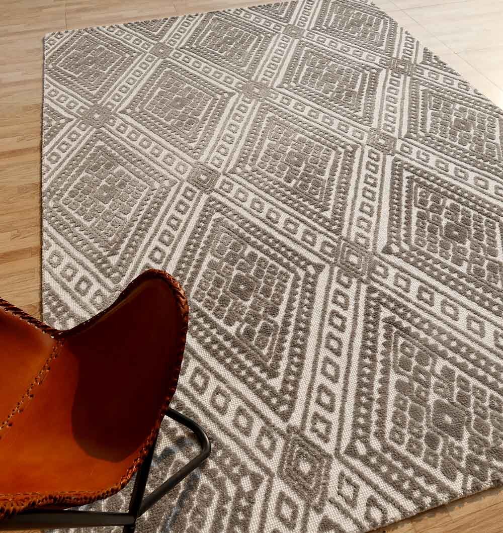The RAMSHA HOME Grey & White Novara Rug - CMN 54 (180x280cm) with a diamond pattern covers a light wooden floor. A brown leather chair with black metal legs is partly seen in the lower left corner.