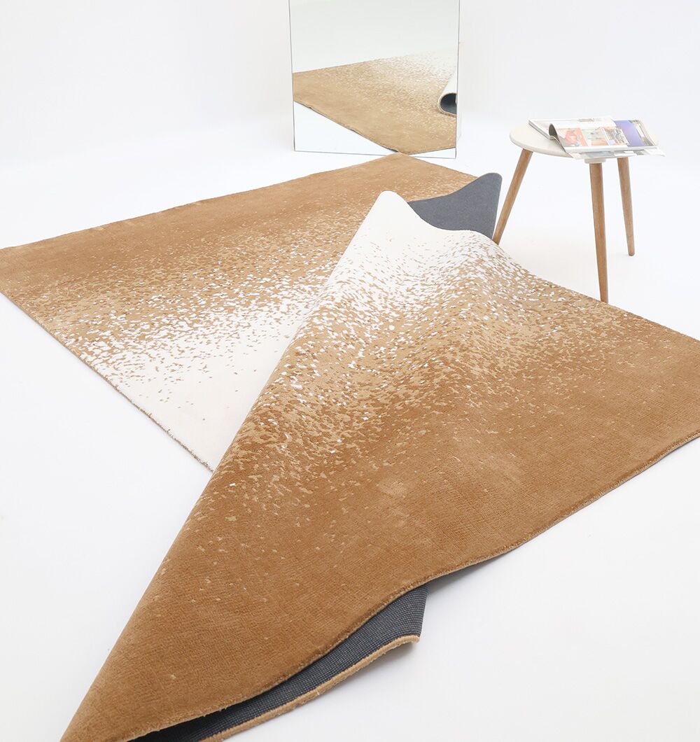 The RAMSHA HOME Rectangle Multi Color Rug - CMN 69 (200x300cm) is partially flipped on a white floor near a round side table with magazines, with a mirror reflecting the modern rug and table in a minimalistic, light setting.
