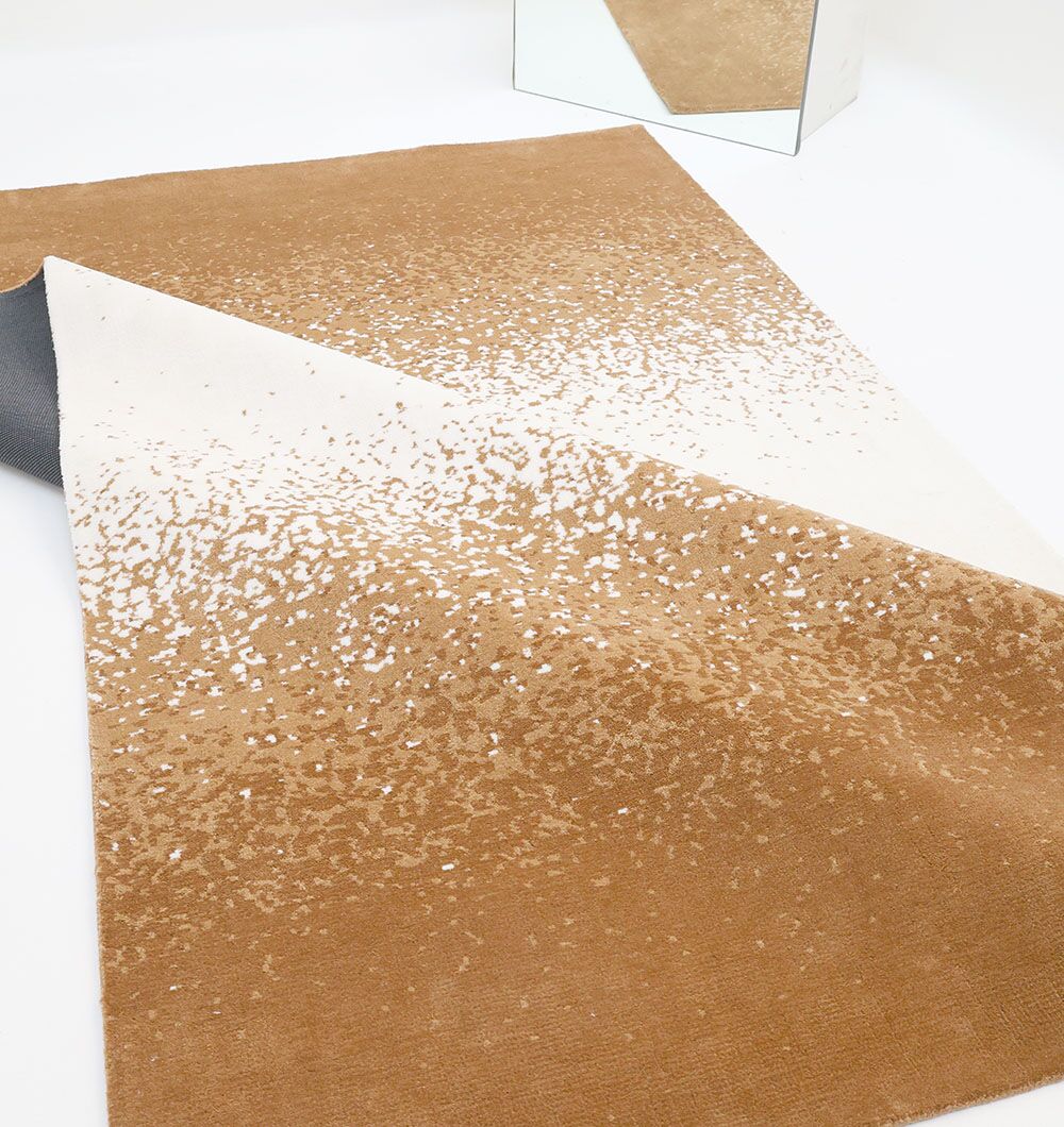 The RAMSHA HOME Rectangle Multi Color Rug - CMN 69 (200x300cm) features a modern ombre gradient in beige, white, and brown. Shown partially folded on a white background, its stylish design is reflected in a mirror at the corner.