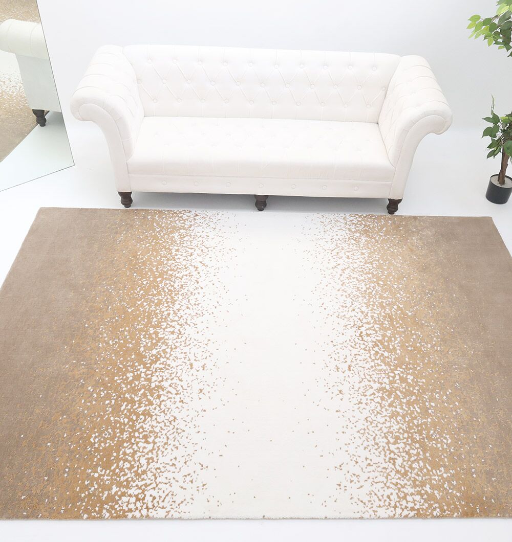 A white tufted sofa sits against a white wall, with the RAMSHA HOME Rectangle Multi Color Rug - CMN 70 (200x300cm) featuring a beige-to-white gradient pattern placed in front. A leafy green plant is nearby.