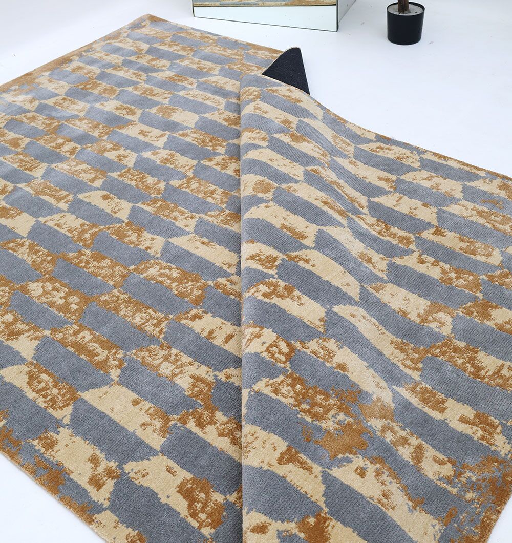 The RAMSHA HOME Home Decor Multi Color Novara Rug - CMN 82, featuring a geometric design in beige, gray, and brown, is partially folded to reveal its underside on a white floor beside a mirror and black planter.