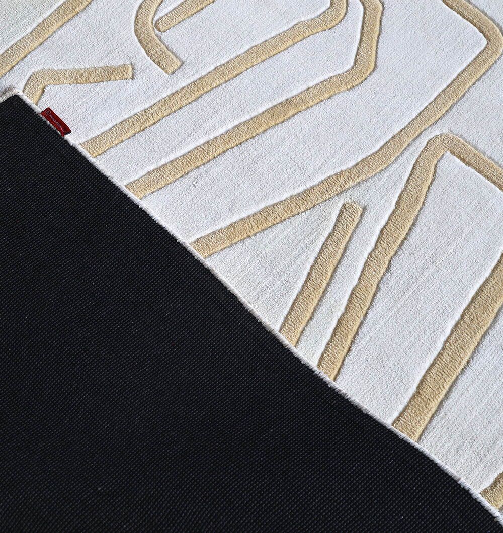 A close-up of the RAMSHA HOME White & Beige Novara Area Rug - CMN 84 (200x300 cm) displays its geometric pattern with raised lines, contrasting beautifully against a solid black backing in this elegant machine-made rug.