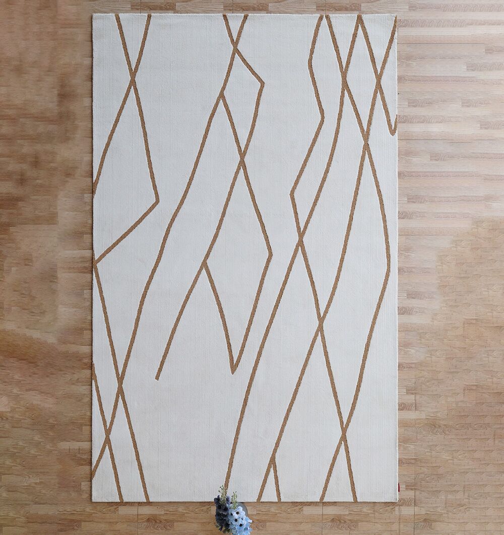 The RAMSHA HOME Novara Area Rug - CMN 87 (200x300 cm), a modern white rectangular rug with thin abstract brown lines, lies on a light wood floor with a small bunch of purple flowers at the bottom center.