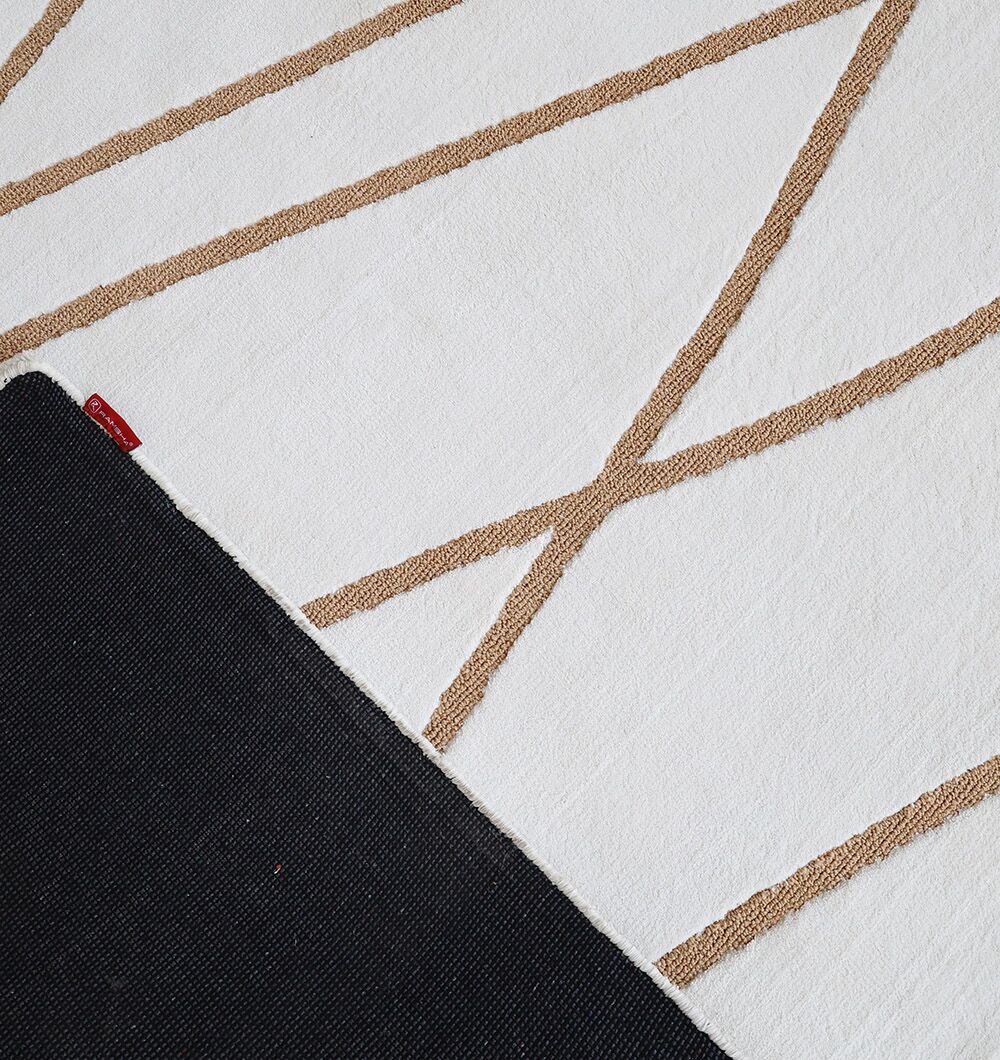 A close-up of the RAMSHA HOME Novara Area Rug (CMN 87, 200x300 cm) shows its white surface with light brown diagonal lines, partially folded to reveal a black non-slip backing and a small red tag.