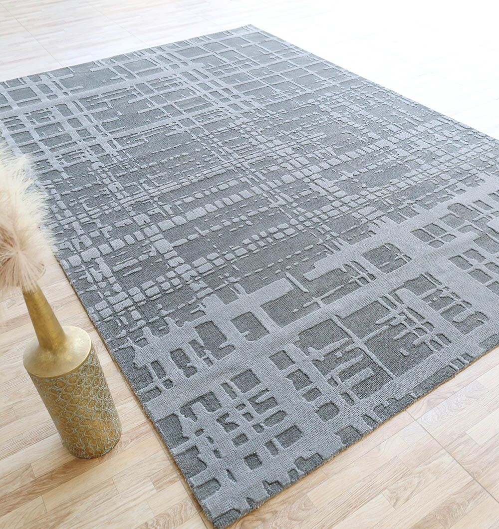 The RAMSHA HOME Decorative Grey Color Novara Rug - CMN 89 (200x300 cm), featuring a modern abstract geometric design, lies on a light wood floor, complemented by a tall golden vase with pampas grass for a stylish look.