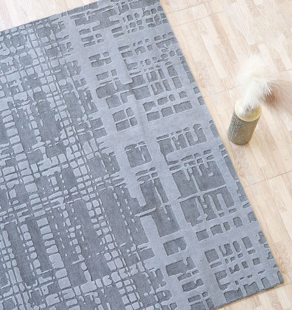 The RAMSHA HOME Decorative Grey Color Novara Rug - CMN 89 (200x300 cm) with a geometric grid pattern lies on a light wood floor, paired with a vase of dried white pampas grass.