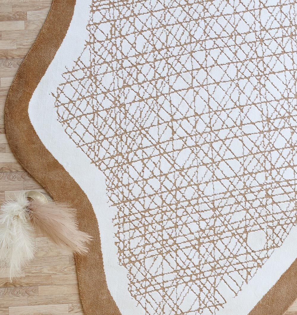 The RAMSHA HOME Novara Shape White & Beige Area Rug (CMN 90, 200x300 cm) features a modern curved design with a tan wavy border and white center accented by abstract crisscrossing tan lines, displayed on light wood flooring with beige pampas grass.