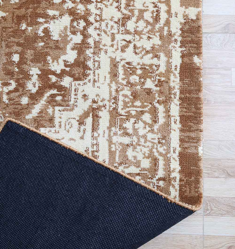 A corner of the RAMSHA HOME Traditional Brown Medallion Novara Carpet - CMN 91 (170x240cm) is flipped, exposing its dark non-slip backing. This machine-made rug lies on a light wooden floor.