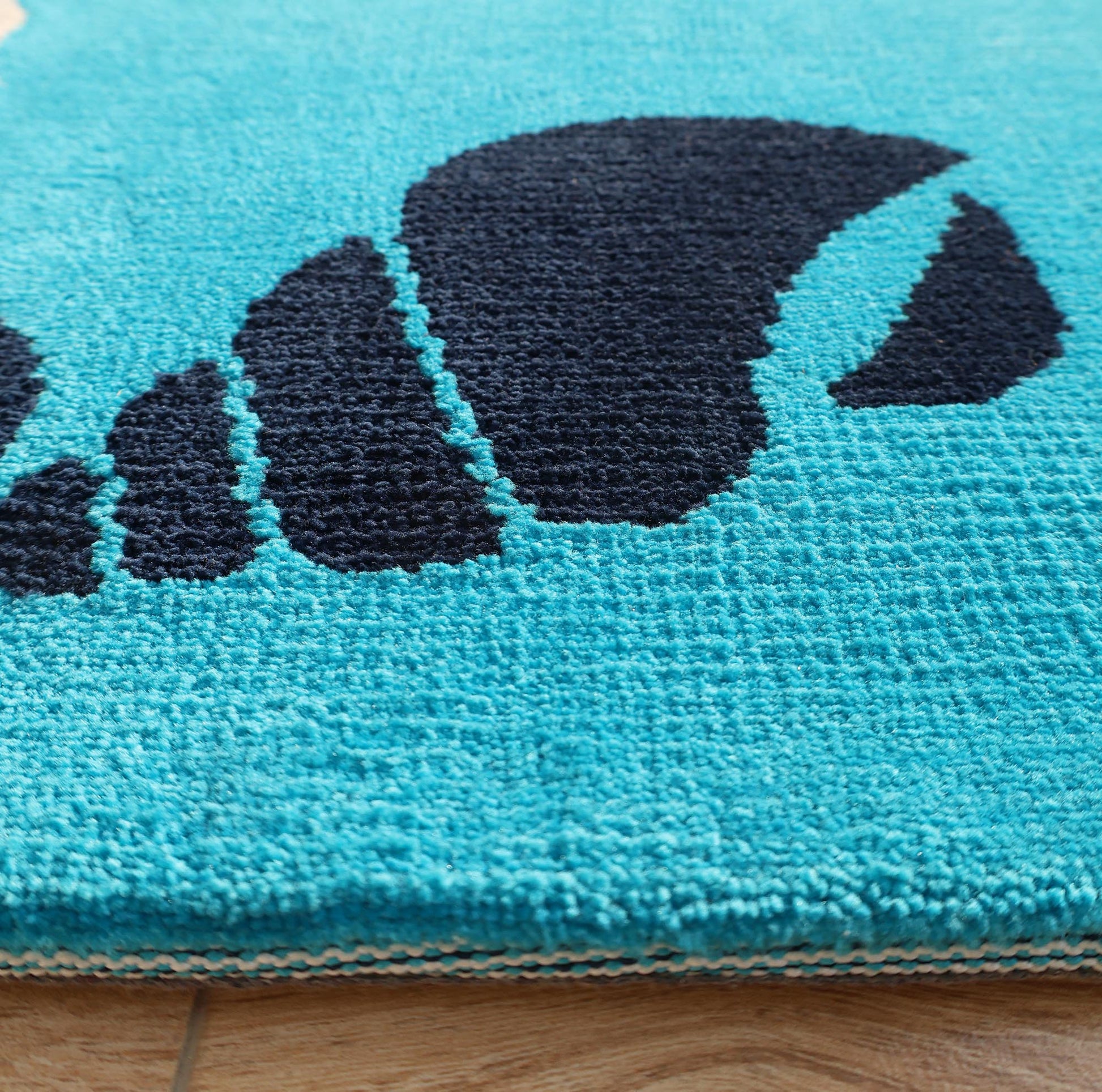 Close-up of the RAMSHA HOME Ultra Soft Ocean Animals Kids Rug (CMN 100, 200x300 cm) featuring a blue ocean-themed texture with a black abstract sea creature design, shown on a wooden floor.