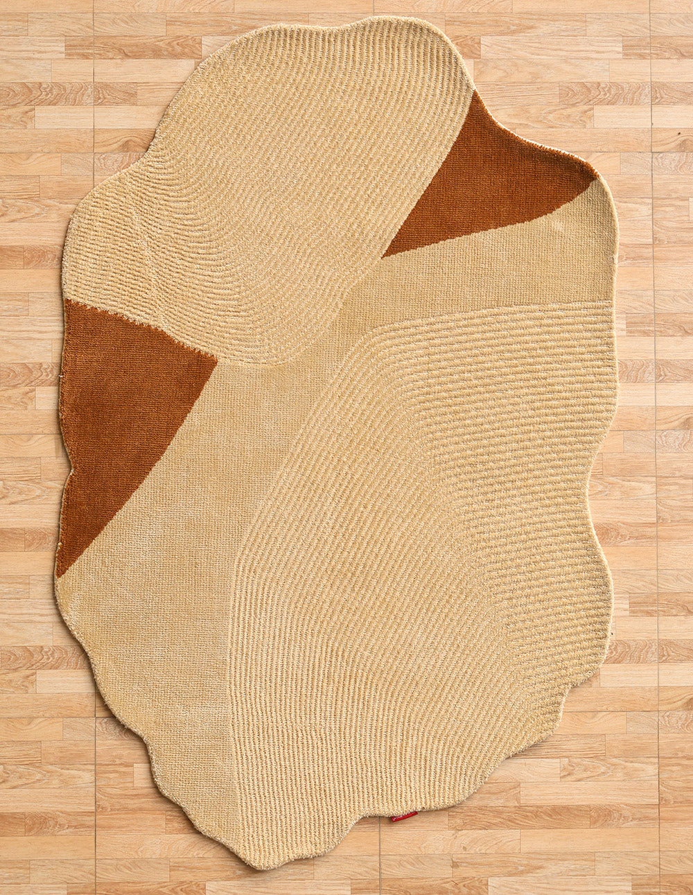 The Dune Flow Abstract Shaped Rug Beige & Terracotta - CMN 102 by RAMSHA HOME rests on a light wood floor, featuring textured, wavy patterns, curved lines, and a blend of smooth and ridged surfaces for modern dimension.