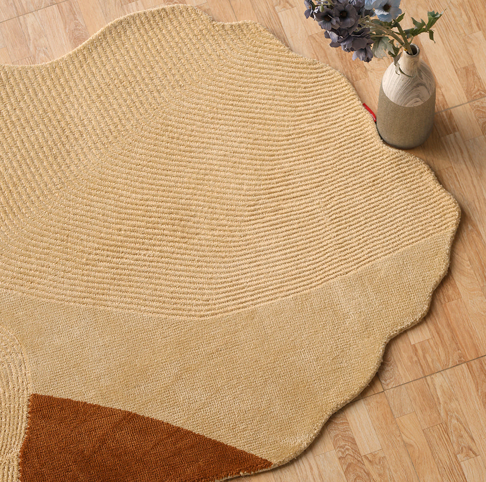The Dune Flow Abstract Shaped Rug in beige and terracotta by RAMSHA HOME (CMN 102), with a scalloped edge and abstract pattern, is on a light wood floor; a vase with purple flowers sits nearby.
