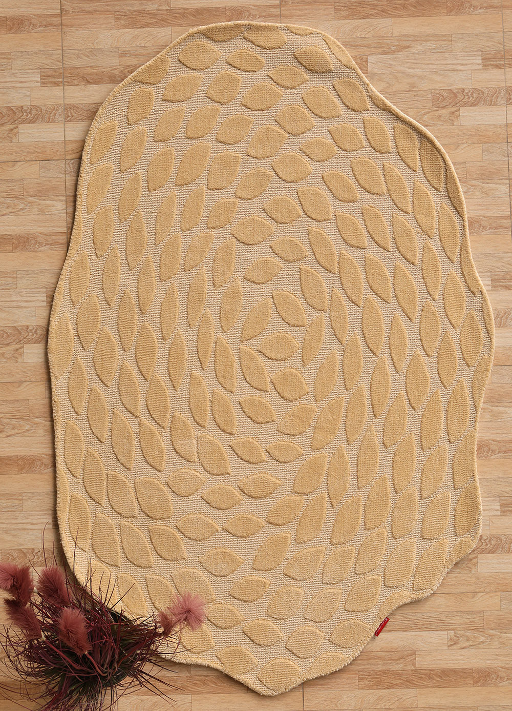 The RAMSHA HOME Autumn Leaf Organic Shaped Rug Beige CMN 103, featuring a swirling leaf pattern, lies on a wooden floor. Burgundy dried flowers in the corner add warmth to the cozy decor.
