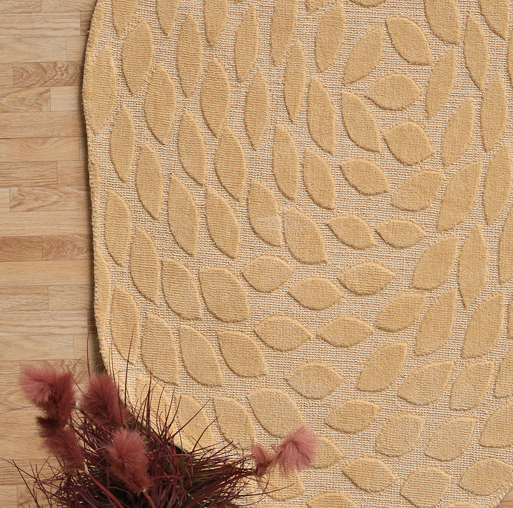 The RAMSHA HOME Autumn Leaf Organic Shaped Rug Beige CMN 103, with a raised leaf pattern, lies on a wooden floor; a vase of dried pinkish-red flowers sits in the bottom left corner.