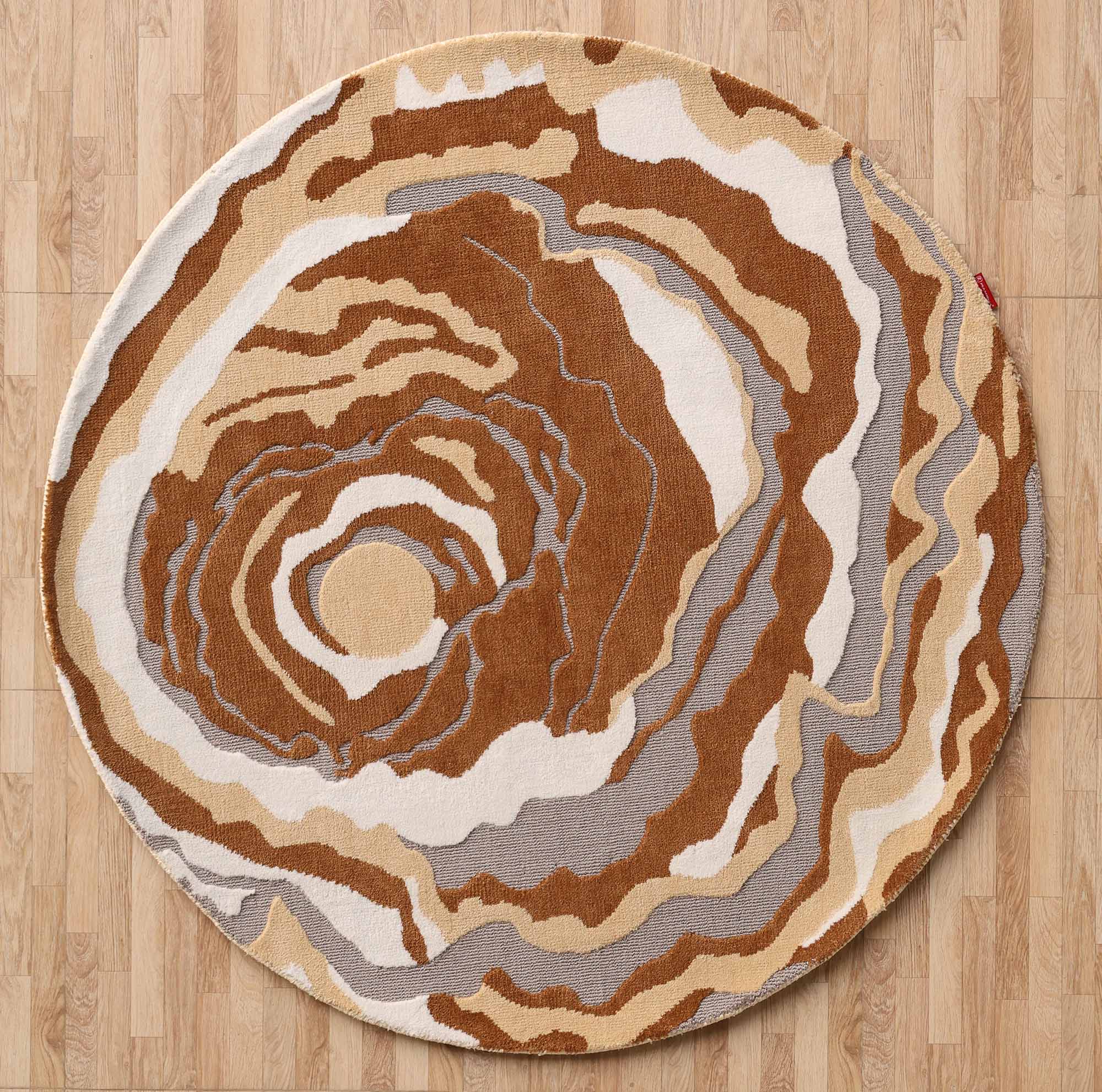 The RAMSHA HOME Modern Round Abstract Rug CMN 104 features swirling patterns in brown, beige, white, and gray, evoking wood grain or geode. It adds a modern touch and sits elegantly on a light wood floor.