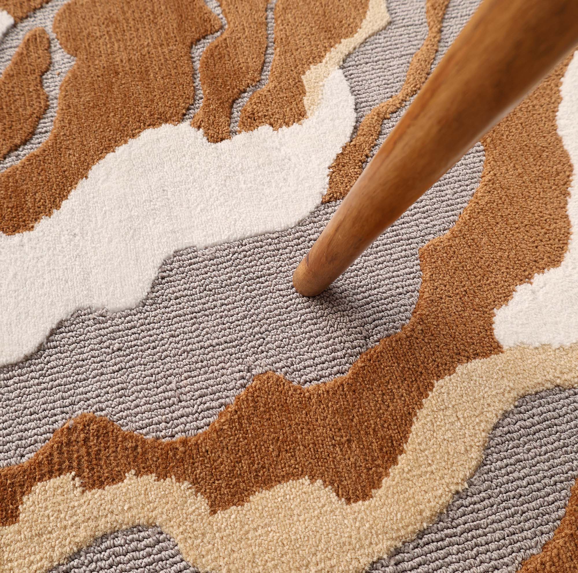 A wooden furniture leg stands on the RAMSHA HOME Modern Round Abstract Rug CMN 104, featuring textured geometric patterns in gray, brown, beige, and white.
