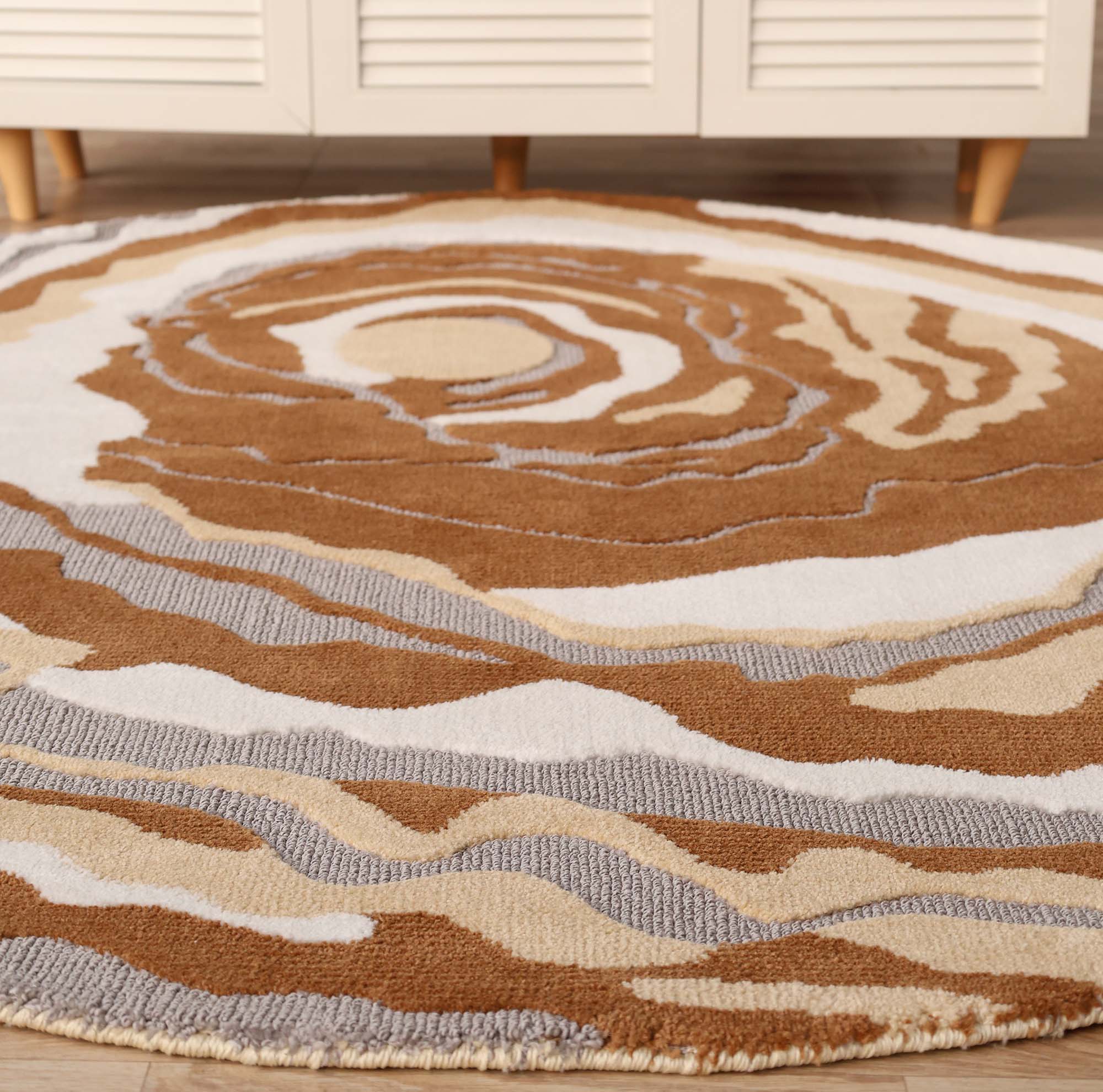The Modern Round Abstract Rug CMN 104 by RAMSHA HOME features a swirling abstract pattern in brown, tan, white, and gray, resembling tree rings, and adds a modern touch to light floors.