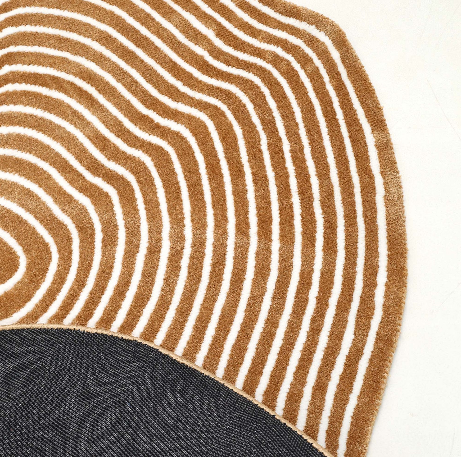 A close-up of the RAMSHA HOME Contour Flow Abstract Shaped Rug – Camel & Ivory CMN 105, featuring modern wavy tan and white stripes curving around a solid dark gray section on a light background.