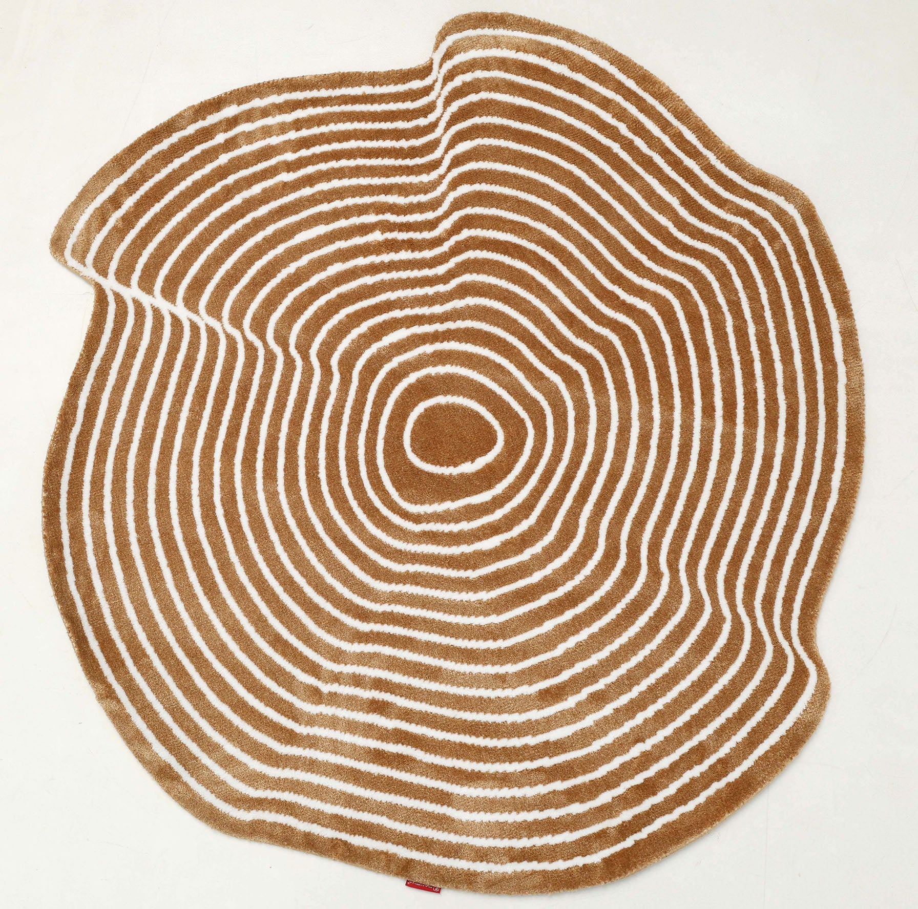 The RAMSHA HOME Contour Flow Abstract Shaped Rug – Camel & Ivory CMN 105 features a tree stump-inspired design with camel and ivory concentric rings, mimicking tree growth rings, set against a plain white background.