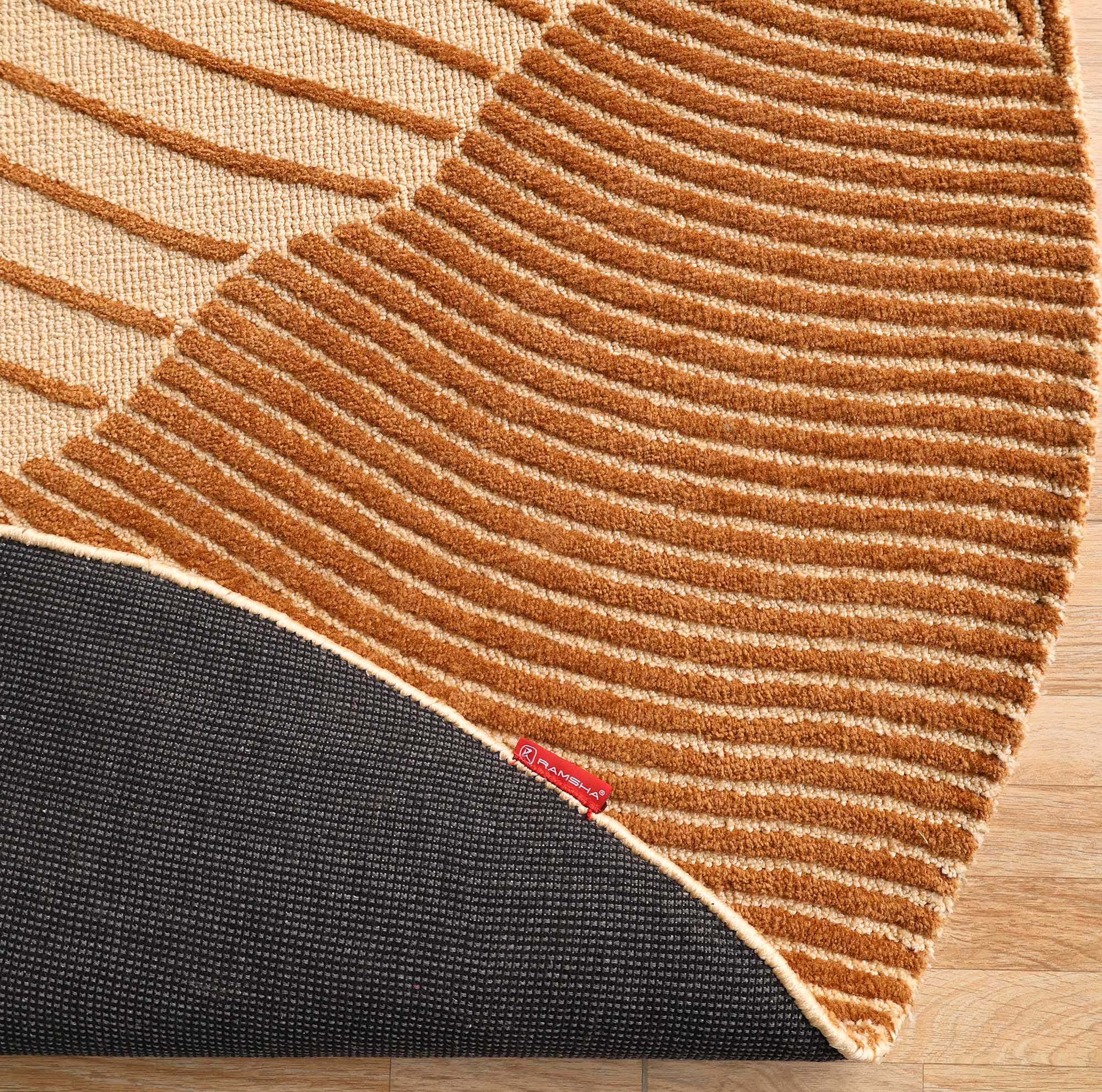 A close-up of the RAMSHA HOME Layered Wave Modern Round Abstract Rug CMN 106, with tan and brown curved stripes, a textured black border, and a small red label, shown on a light wooden floor.