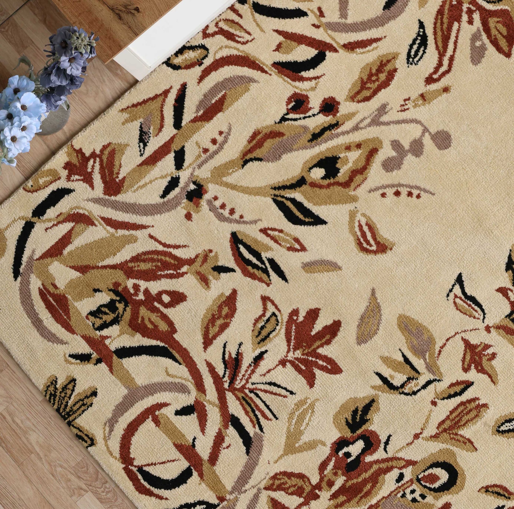 The RAMSHA HOME Vintage Floral Elegance Handmade Rug 200x300 CM - CMN 111, featuring an abstract floral pattern in warm tones, is displayed on a wooden floor beside a vase of purple hydrangeas.