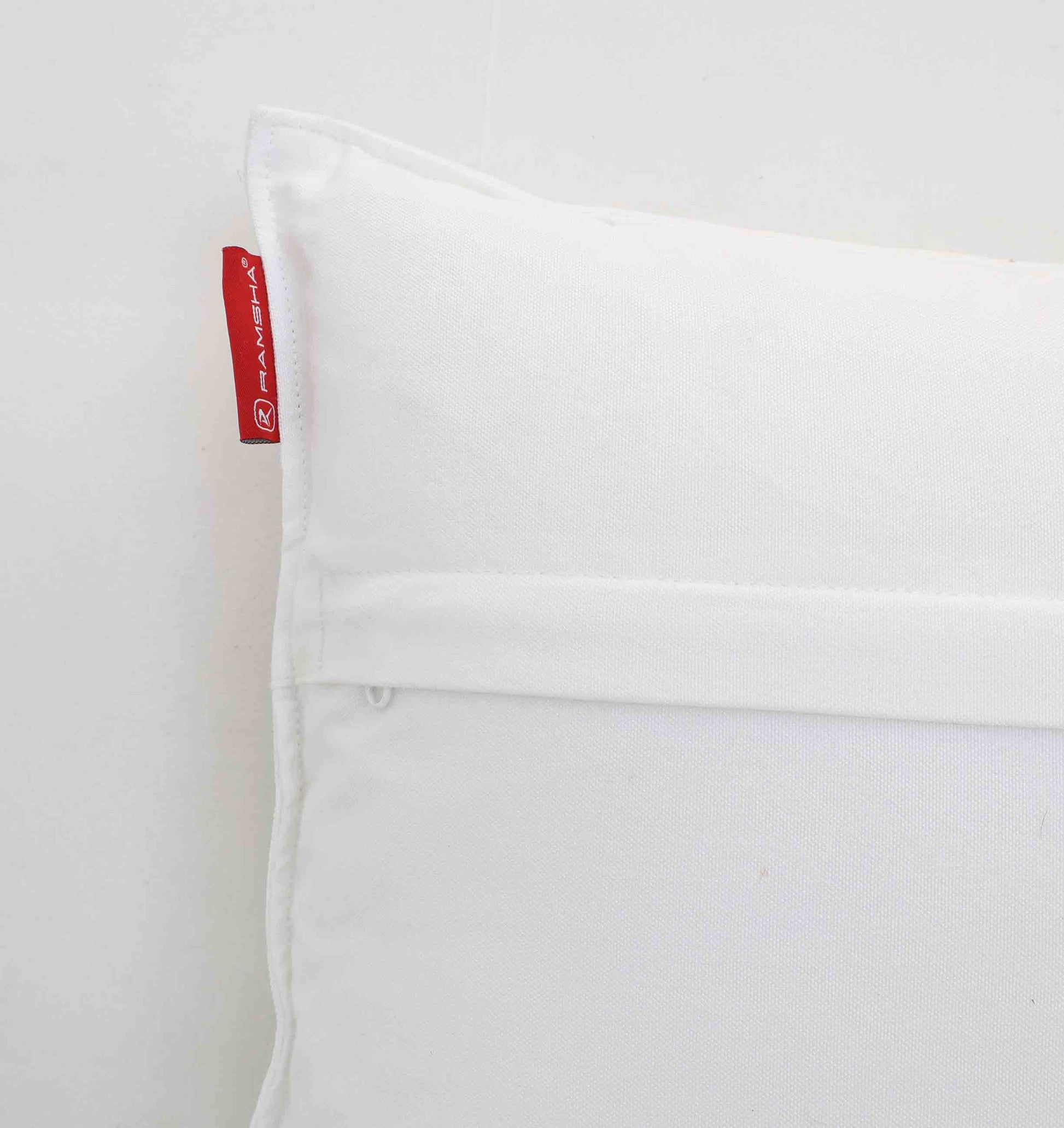 Close-up of the White Color Decorative Cushion For Sofa - CS 293 by Ramsha Home, featuring a horizontal flap and red fabric tag on the left edge, displayed against a plain white background.