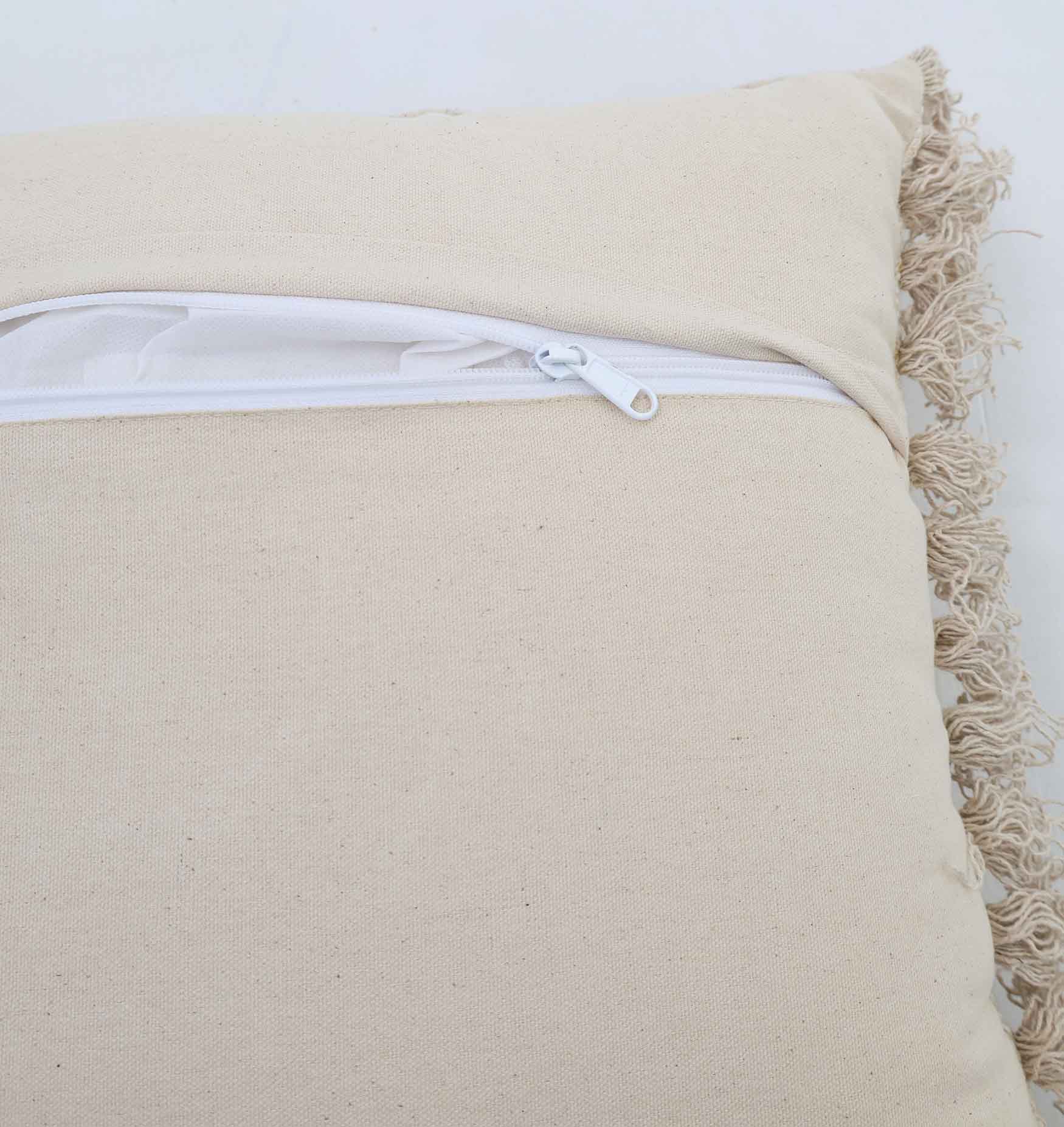 A close-up of the Ramsha Home Natural Color Cushion - CS 295 (45x45cm), featuring a white zipper, inner lining, plain fabric surface, and a textured fringe on one side—perfect for stylish home decor.