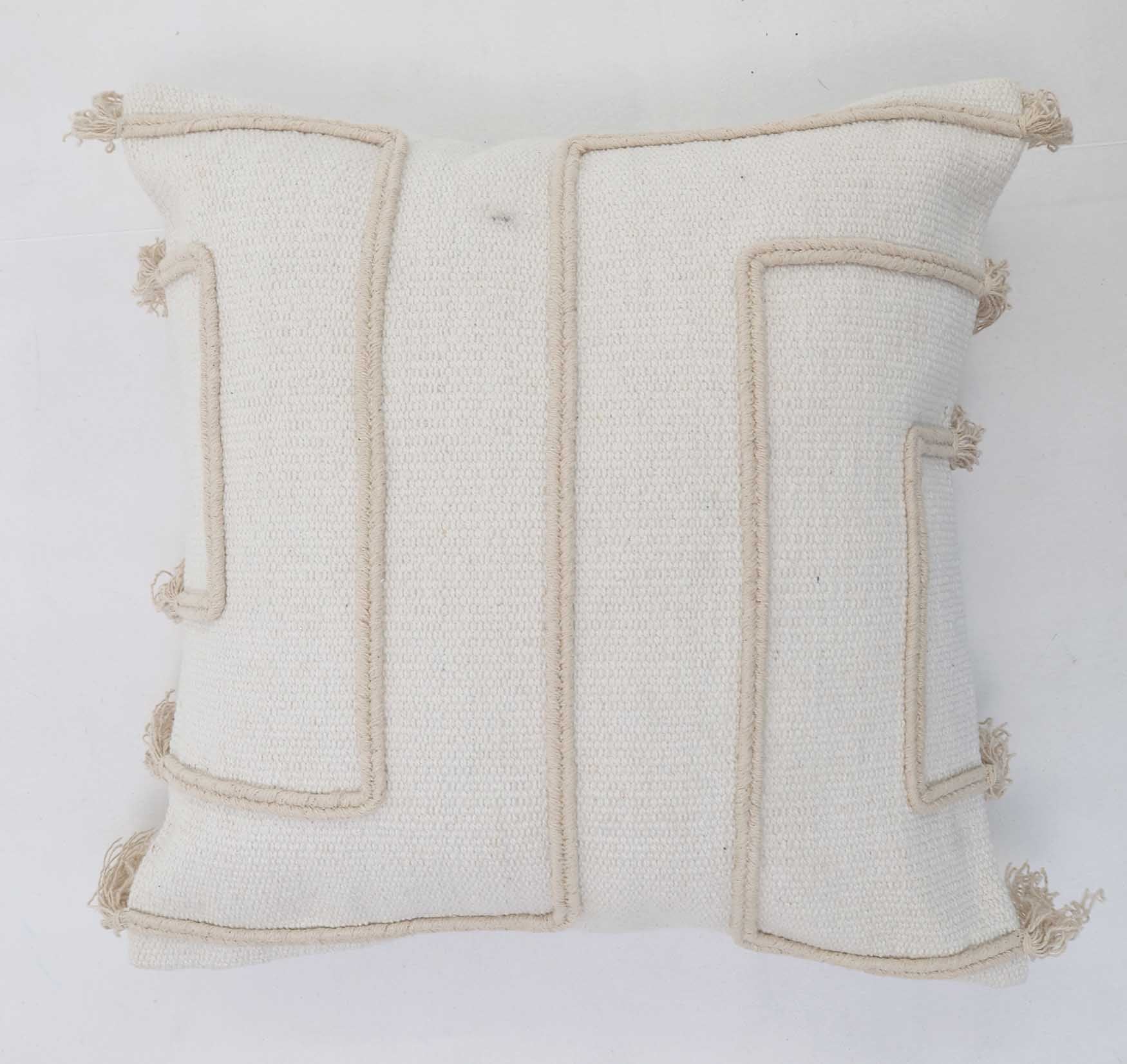The Ramsha Home Cotton Cushion Natural & White Color - CS 299 (45x45cm) features beige raised geometric patterns and tassels, blending elegance with modern home decor—luxury furnishings from a top UAE brand.