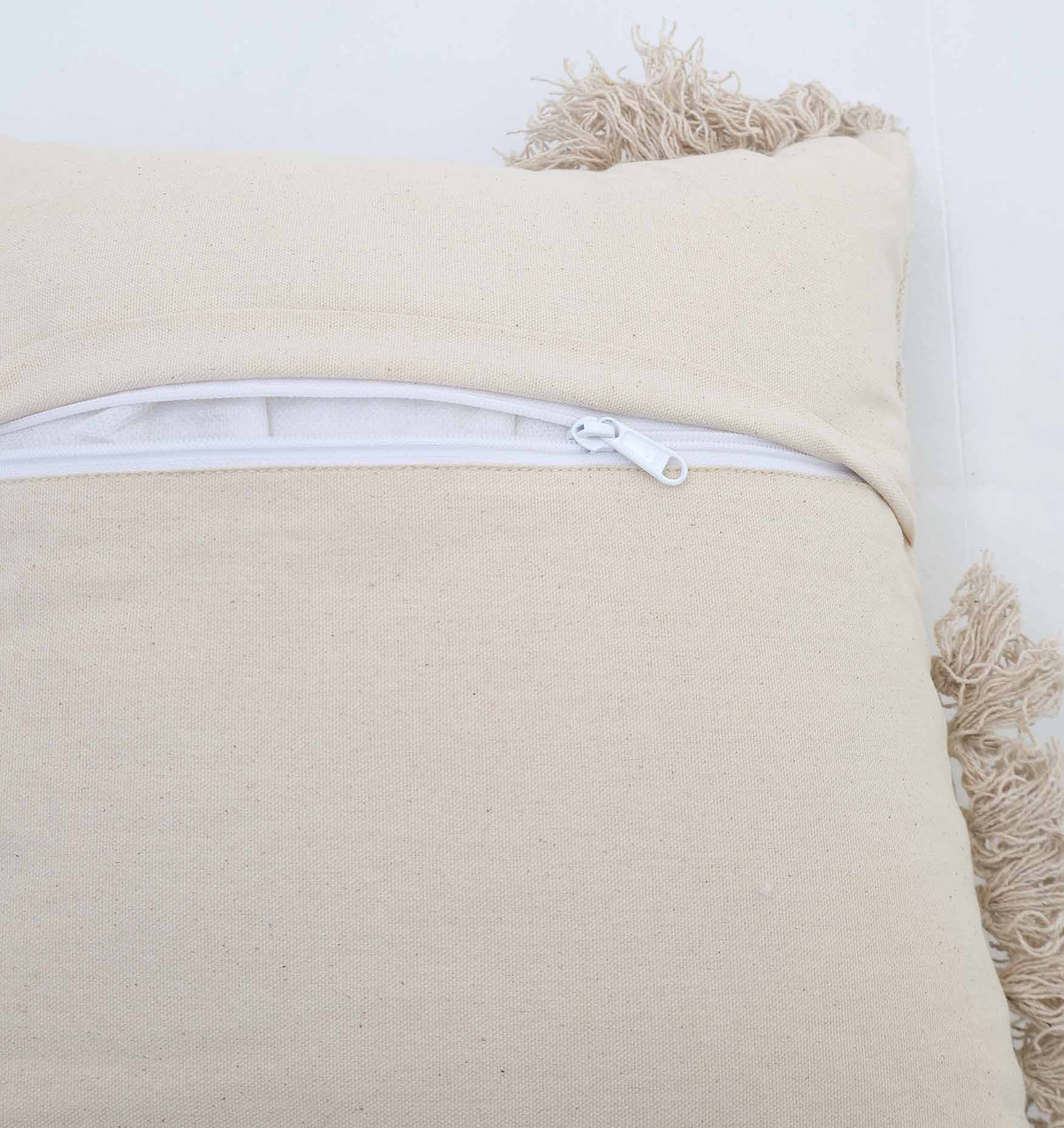 A close-up of the Ramsha Home 45x45cm Home Decor Cushion Natural Color - CS 302 shows its beige shade, fringed tassels on one side, and a white zipper at the back partially open to reveal the inner lining.